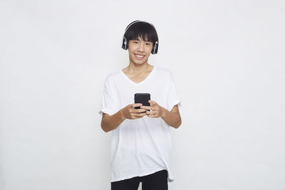 Full length of smiling young man using mobile phone against white background