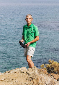 Senior man standing on rock against sea