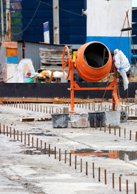A large construction orange mortar mixer stands against the backdrop of concrete road repair work