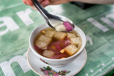 Cropped hand of person having indonesian dessert from bowl at table