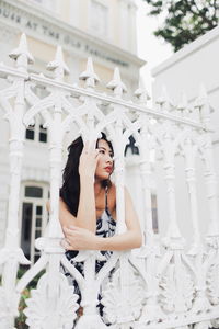 Young woman looking away while standing by fence