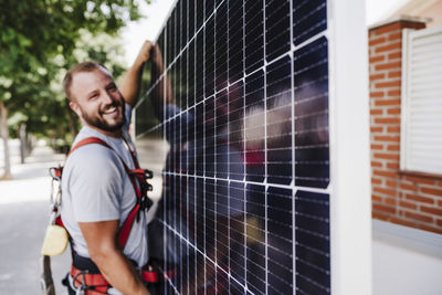 Smiling technician carrying heavy solar panel
