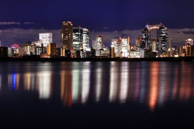 Illuminated buildings by lake against sky in city at night