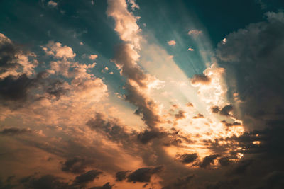 Low angle view of sunlight streaming through clouds