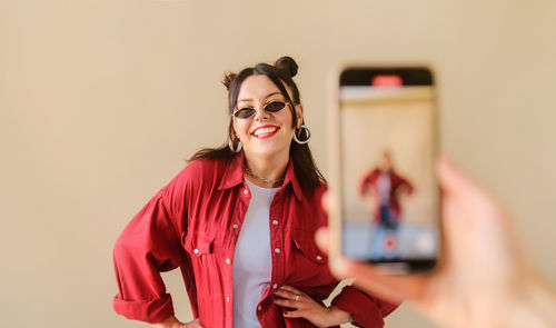 Young woman using mobile phone while standing against wall