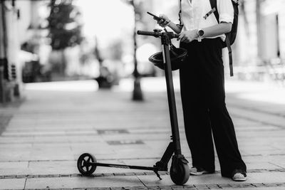 Businesswoman standing and using her smart phone with electric scooter next to her in the city.