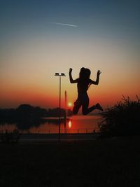 Silhouette man jumping against orange sky