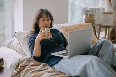 Young woman using phone while lying on bed at home