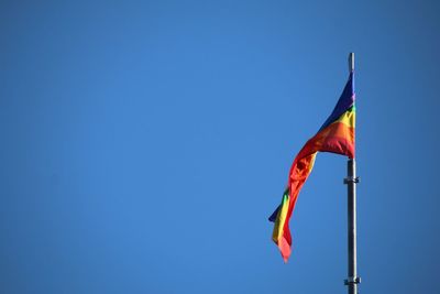 Rainbow flag waving against clear blue sky