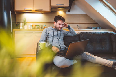 Young woman using laptop while sitting on sofa at home
