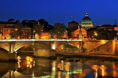 Illuminated bridge over tiber river against blue sky