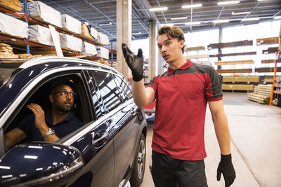 Male sales staff assisting customer sitting in car at hardware store