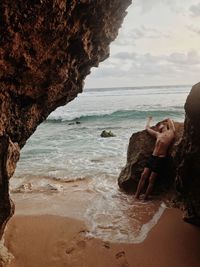 Full length of man on rock at beach against sky