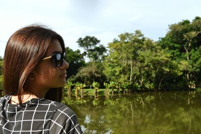 Young woman wearing sunglasses at lake against trees
