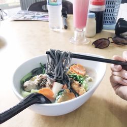 Cropped hand holding chopsticks with noodles over table