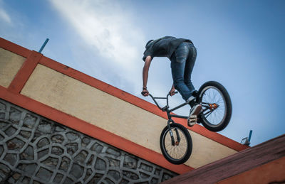 Low section of man performing stunt on bicycle against blue sky