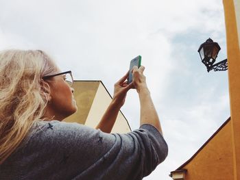 Low angle view of woman photographing with mobile phone against sky