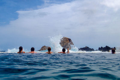 People looking at water splashing against rocks in sea