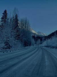 Road amidst trees against clear blue sky during winter