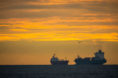 Silhouette ship sailing on sea against orange sky