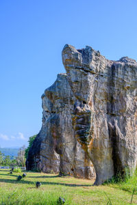 Low angle view of rock formation on field against clear blue sky
