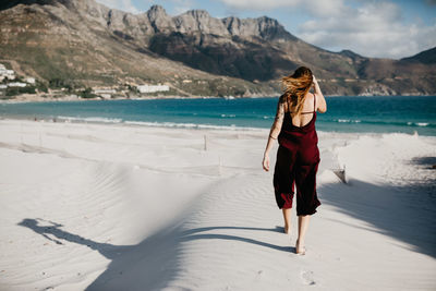 Rear view of woman walking at beach against mountain