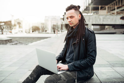 Young man looking at camera while sitting on mobile phone