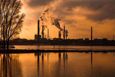 Smoke emitting from factory against sky at sunset