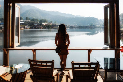 Rear view of woman standing on table by lake