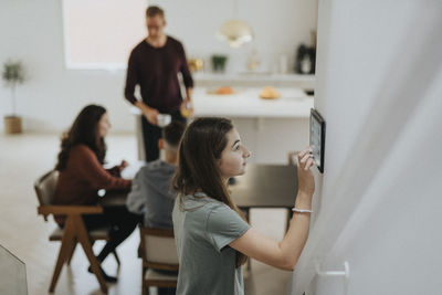 Pre-adolescent girl using digital tablet mounted on wall by family at modern home