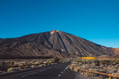 Road by mountain against clear blue sky