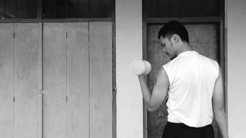 Side view of young man standing against wooden wall