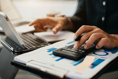 Midsection of businessman using calculator at table