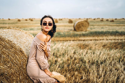 Portrait of young woman with hay bales on field