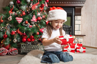 Cute girl holding gift box by christmas tree at home