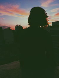 Rear view of silhouette woman standing against sky during sunset