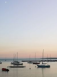 Sailboats moored in sea against clear sky during sunset