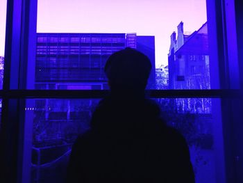 Rear view of silhouette man looking through window in building