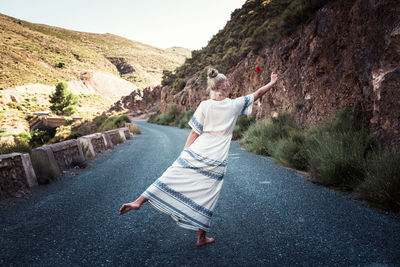 Rear view of teenage girl standing on one leg while holding rose on road