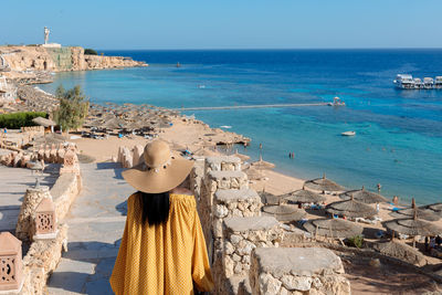 Happy african american woman in yellow dress and sun hat enjoys view of coast of red sea on natural 