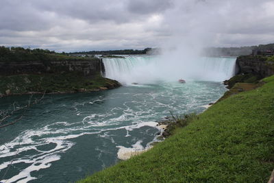 Scenic view of waterfall against cloudy sky