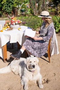 A woman in a hat is sitting on a chair near the table, a labrador retriever is lying next to her