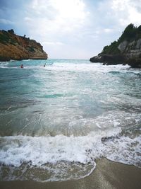 Scenic view of beach by rocks against cloudy sky