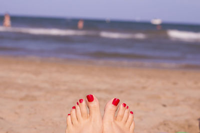 Low section of woman with red nail polish at beach