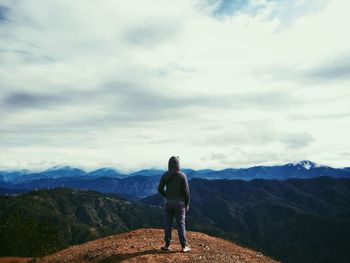 Rear view of man standing on mountain peak against sky