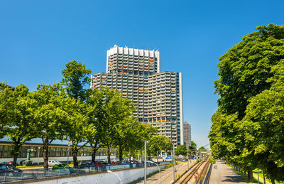 Road by trees and buildings against clear blue sky