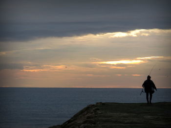 Silhouette of man with fishing rod against sea