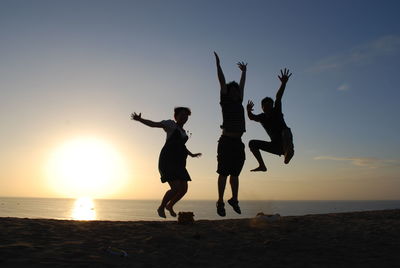 Silhouette people at beach against sky during sunset