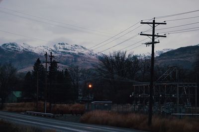 Electricity pylon by trees against sky