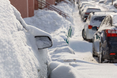 Row of snow drifted cars in a row along the street near residential building at winter day snowfall